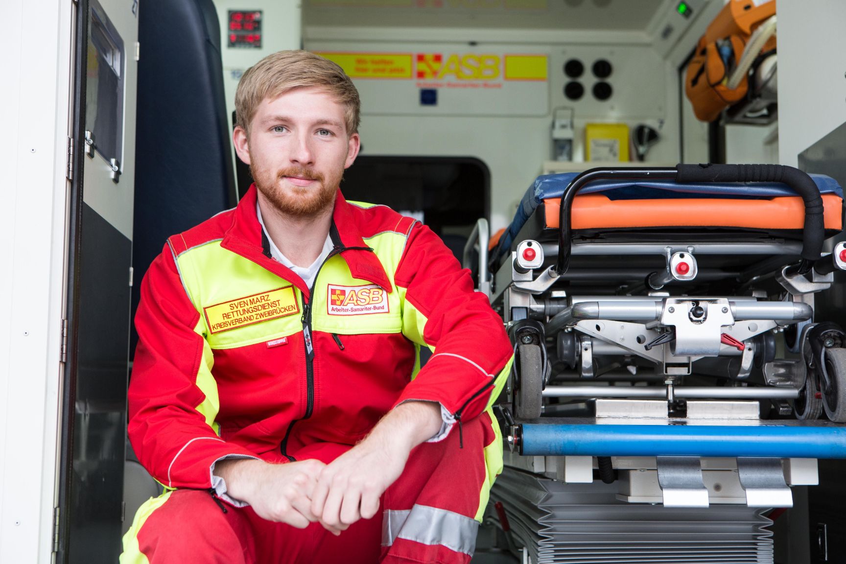 Der Rettungswagen ist einsatzbereit und die Ausrüstung vollständig. Jetzt entspannt sich der angehende Notfallsanitäter kurz und sitzt in der geöffneten Tür vom im Rettungswagen